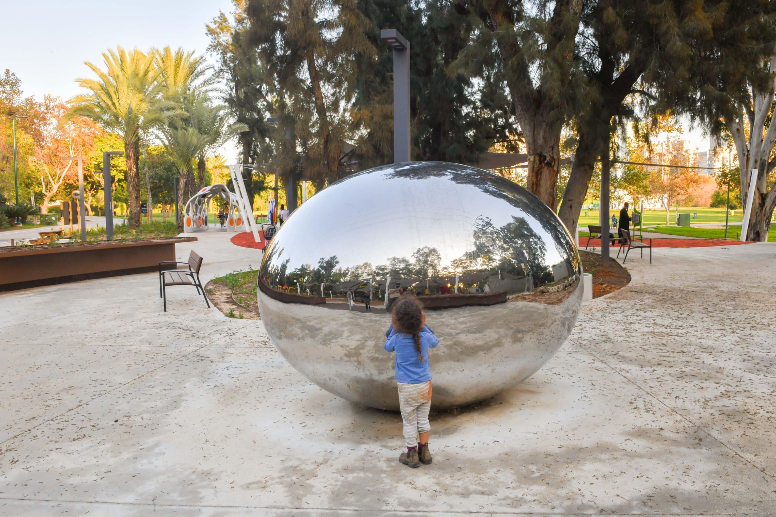 מתקן בצורת ביצה שוכבת ועשויה חומר דמוי מראה וילד קטן מתבונן בה מקרוב