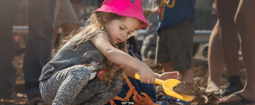 ילדה בכובע ורוד חופרת בכף צהובה