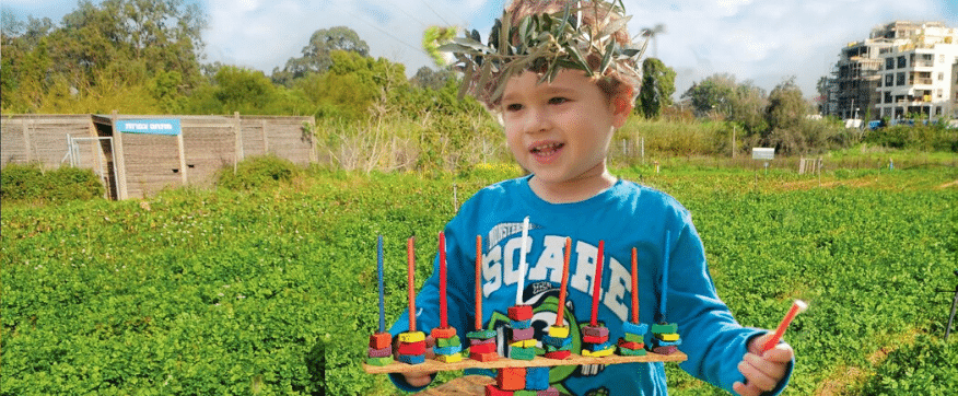 ילד מדליק חנוכיה על רקע שדות ירוקים