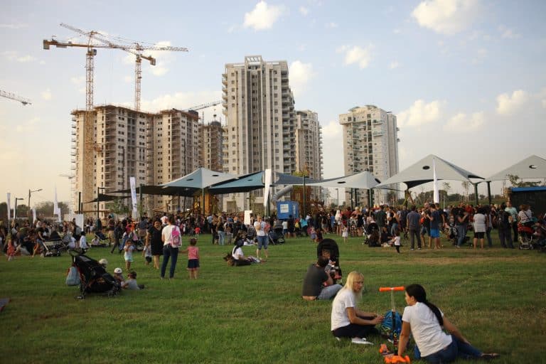 אנשים על הדשא בפארק על רקע בנייני השכונה