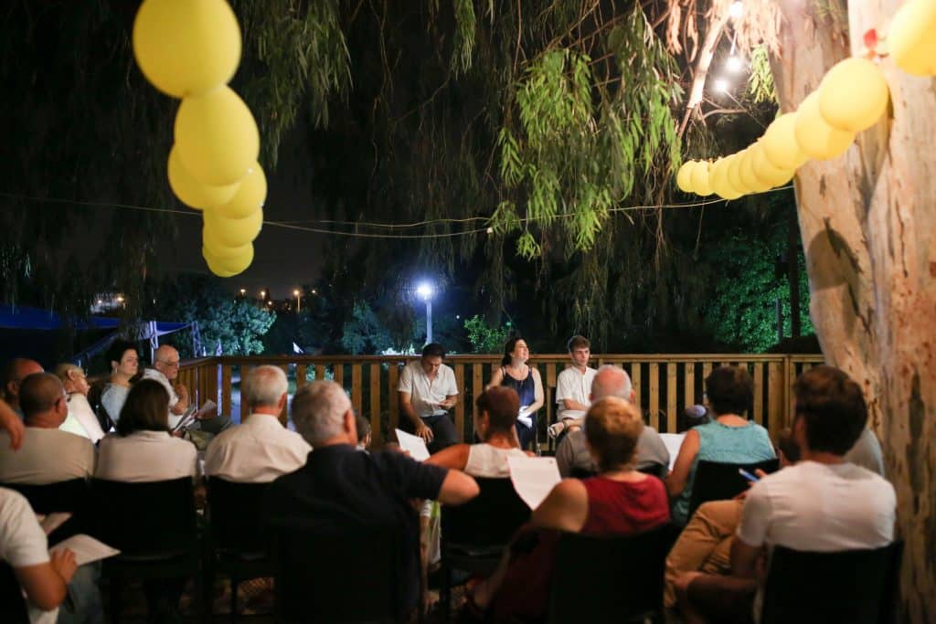 בלונים בחצר מעל לקבוצת אנשים שיושבת ומאזינה