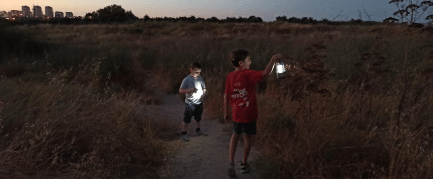 שני ילדים אוחזים בעששיות בחשיכה על תל נפוליאון