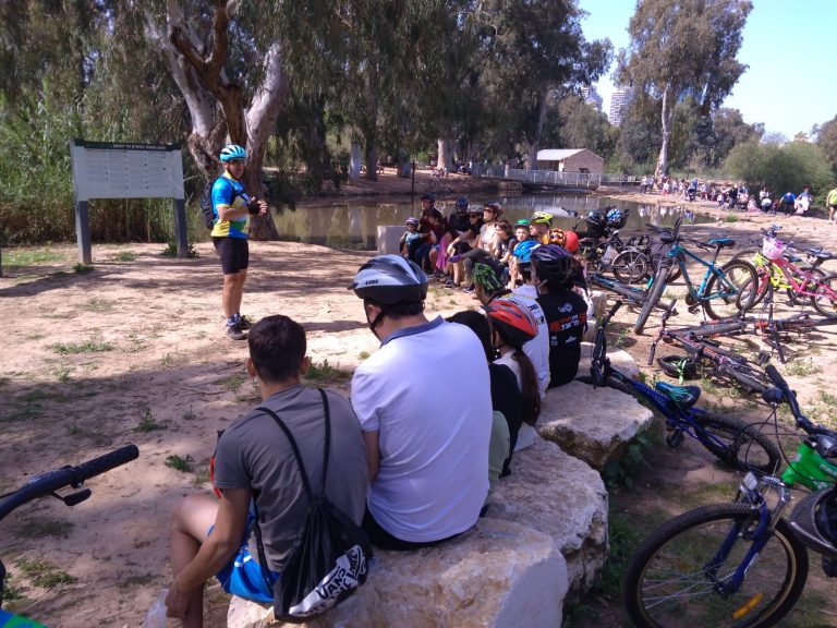 קבוצת רוכבים יושבים ומקשיבים למדריך ליד שבע טחנות