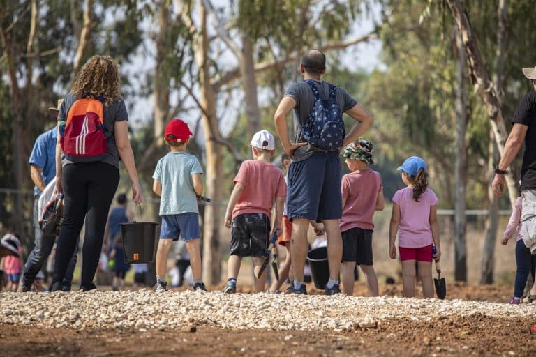 קבוצה אנשים וילדים מאזינה להדרכה ליד העצים