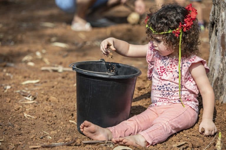 ילדה קטנה עם זר פרחים יושבת על החול וממוללת בידיה חול לדלי