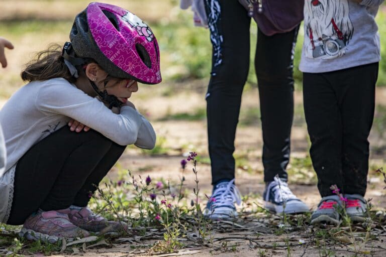 ילדה מתכופפת ומתבוננת בפרח