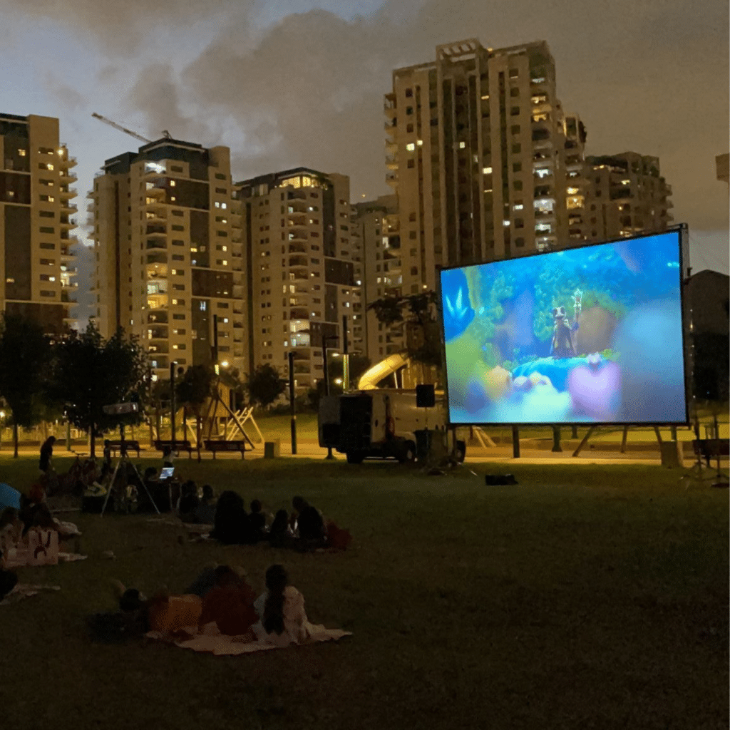 אנשים צופים בסרט על הדשא, על רקע בנייני העיר