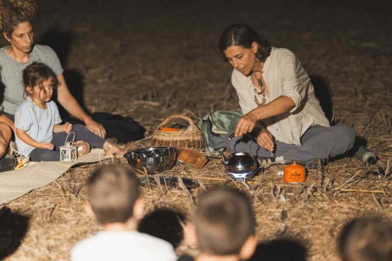 מדריכה יושבת על באדמה ומכינה תה על גזיה