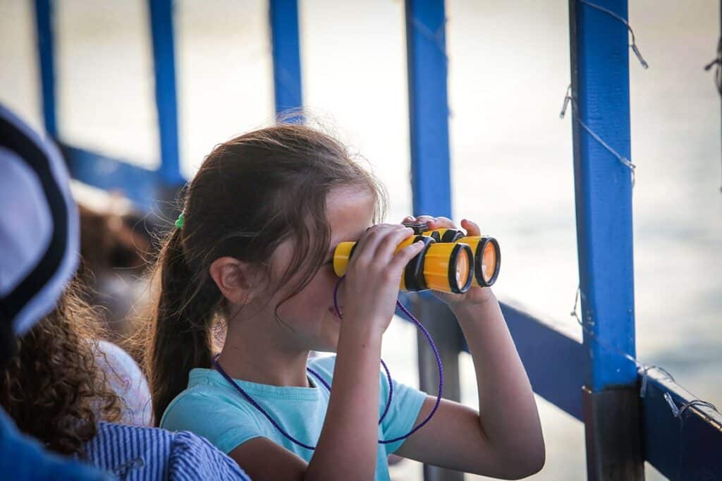 ילדה מביטה דרך משקפת על האגם