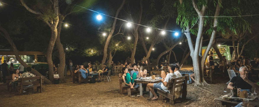 קבצת אנשים מבלים תחת עצים ותאורת גרילנדות