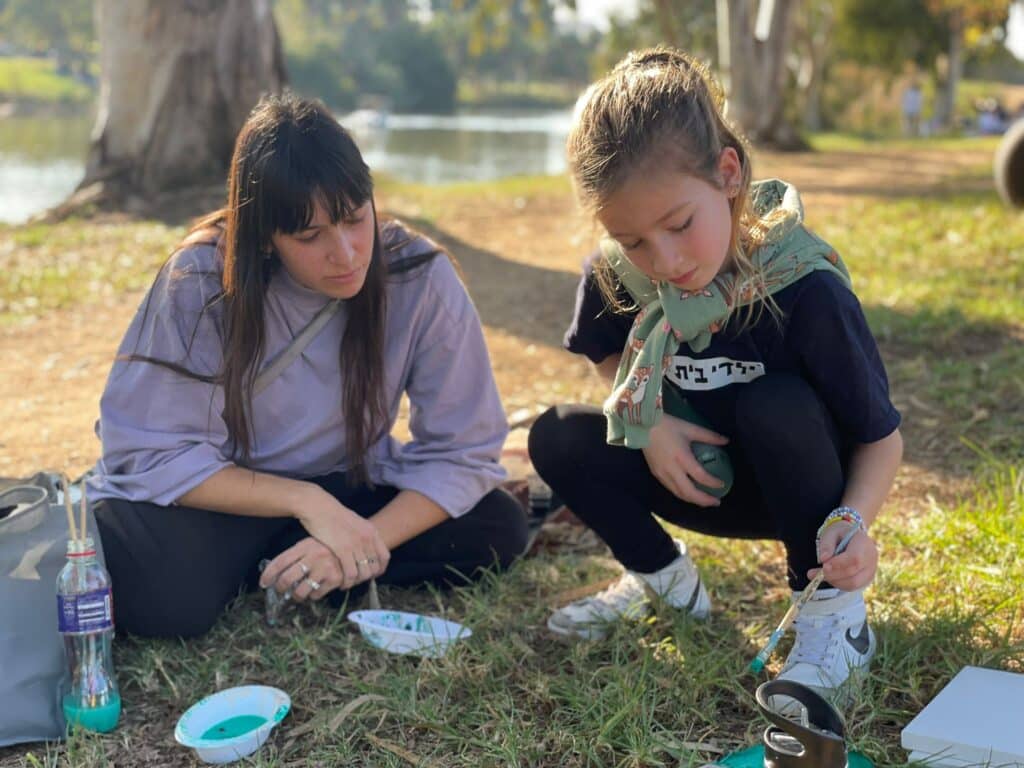 נועה המדריכה מסבירה לילדה כיצד לעבוד על הציור שלה