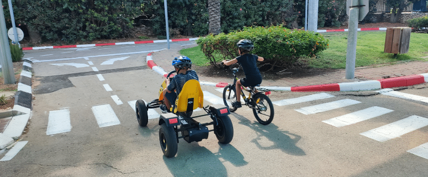 שני ילדים רוכבים על קארטינג ועל אופניים במרכז דמוי כביש