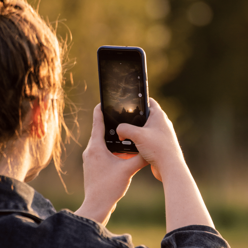 נערה אוחזת בנייד ומצלמת שקיעה