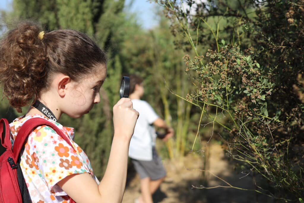 ילדה מביטה דרך זכוכית מגדלת בשיח