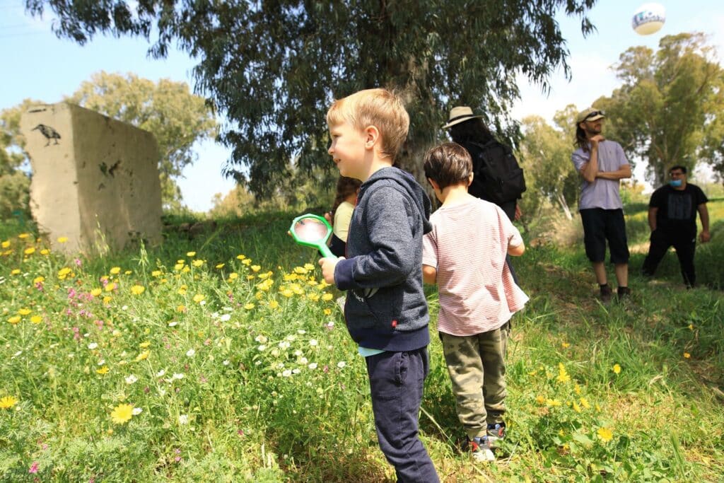 ילד עומד בשדה פורח ובידו זכוכית מגדלת גדולה וירוקה