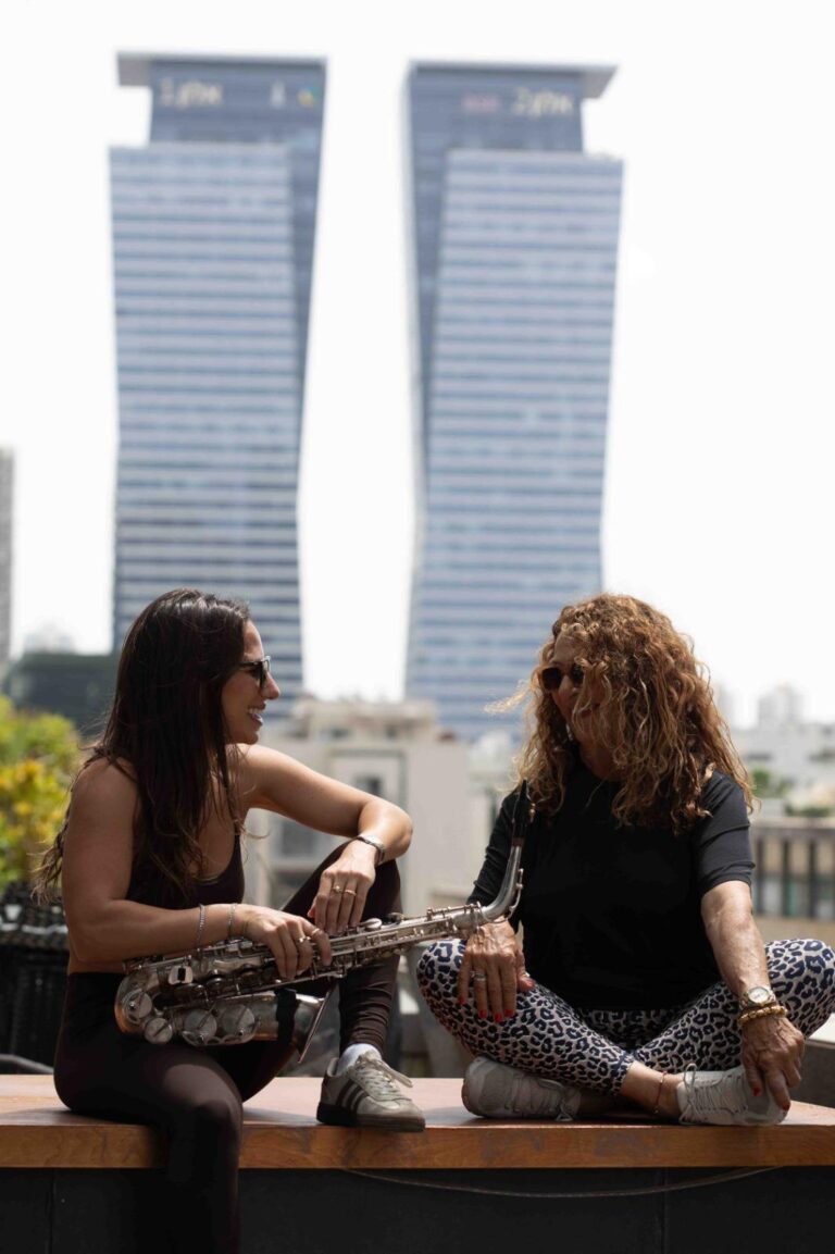 שתי נשים יושבות על גדר בבגדים ספורטיביים על רקע מגדלי משרדים