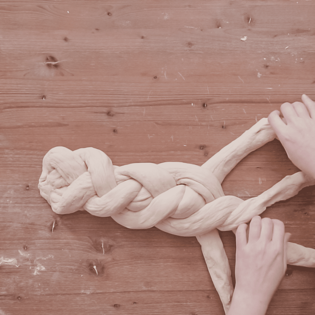 ידיים קולעות חלה על שולחן עץ