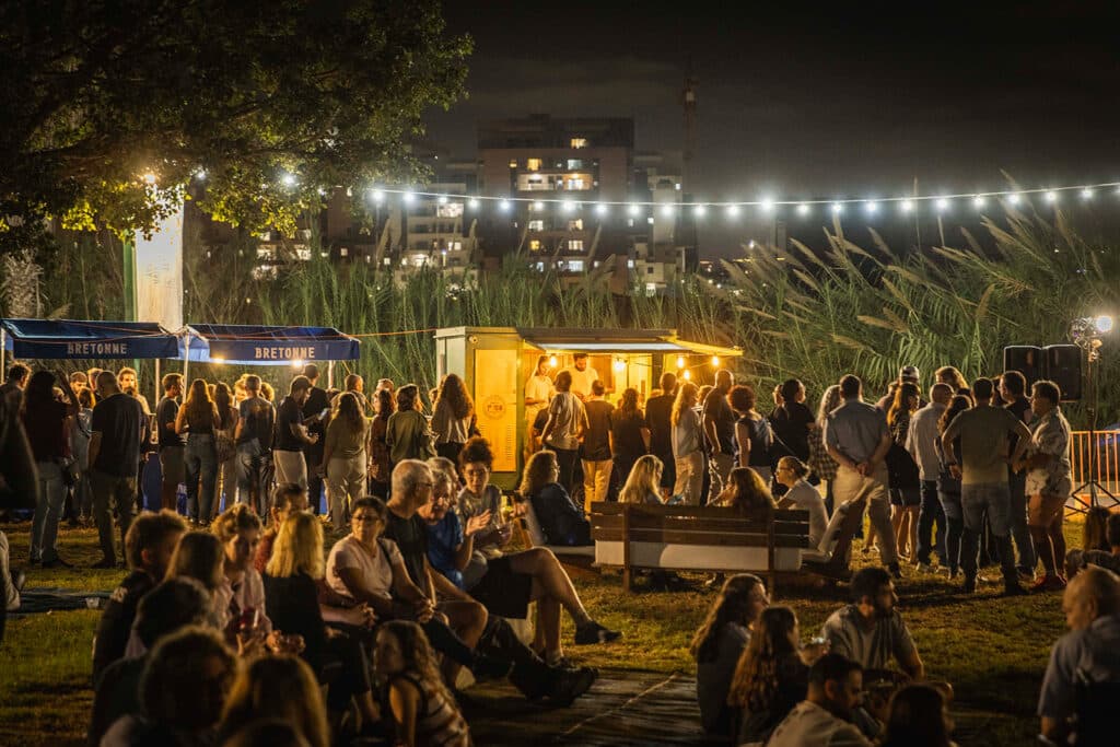 אנשים באירוע, עומדים על דשא ליד דוכן יין ושרשראות אורות מלמעלה