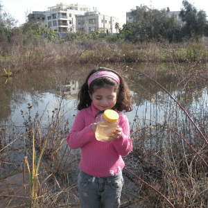 ילדה בוחנת צנצנת מים בזכוכית מגדלת